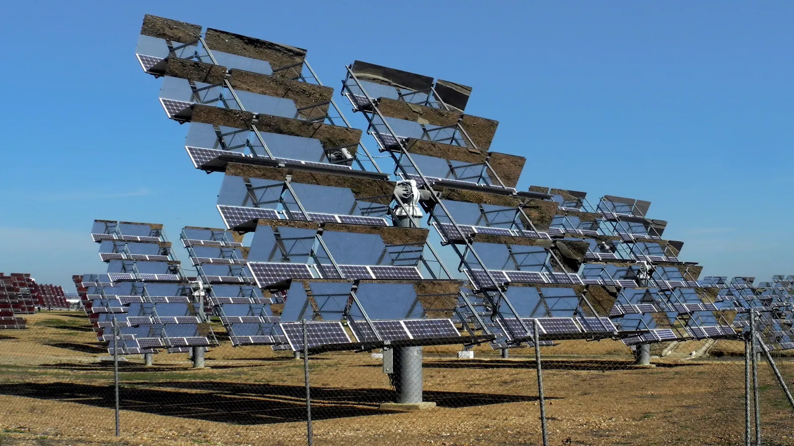 Paneles solares fotovoltaicos sobre seguidores en una planta solar de Sanlúcar la Mayor (Sevilla), bajo un cielo azul despejado.