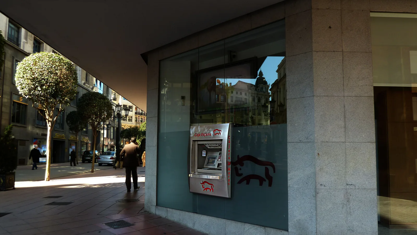 Cajero automático empotrado en la fachada acristalada de un edificio de granito, junto a una acera por la que pasan peatones, en una imagen de 2012.