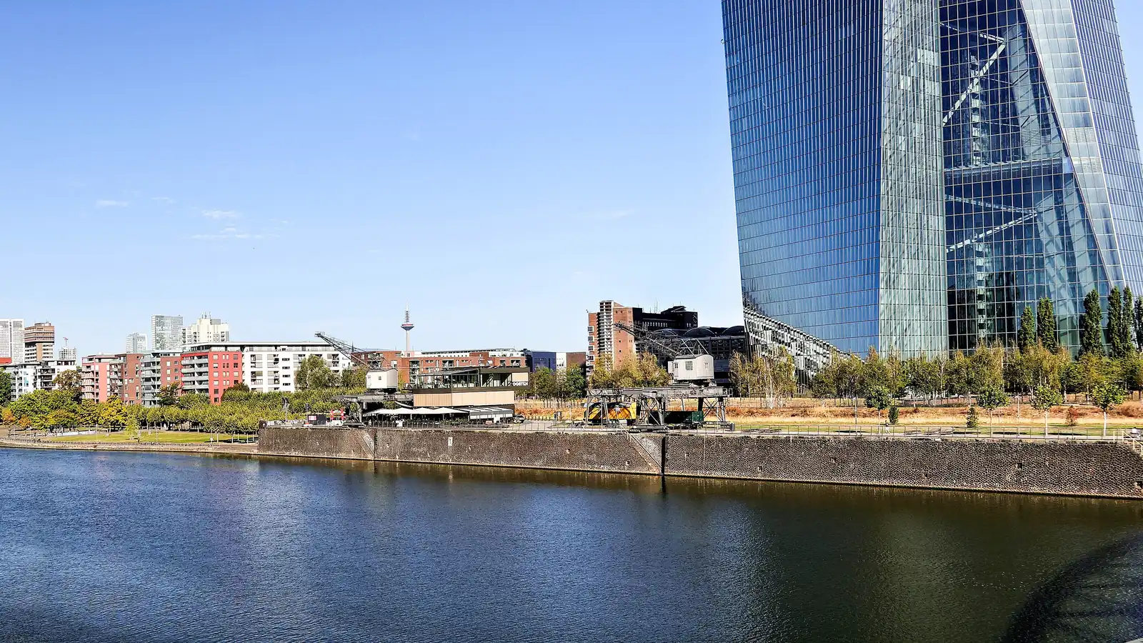 Torre de cristal de la sede del Banco Central Europeo junto al río Meno, en Fráncfort, con cielo azul.